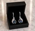Sapphire Blue Teardrop and CZ Swirl Huggie Drop Earrings in silver displayed in a black luxury gift box