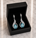 Aqua Blue Topaz Teardrop and CZ Swirl Huggie Drop Earrings in silver displayed in a black luxury gift box